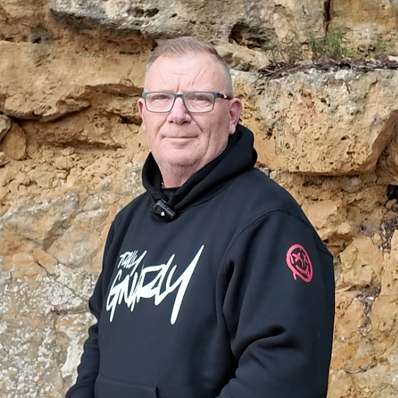 Man wearing a black hoodie with 'Totally Gnarly' text against a stone wall.