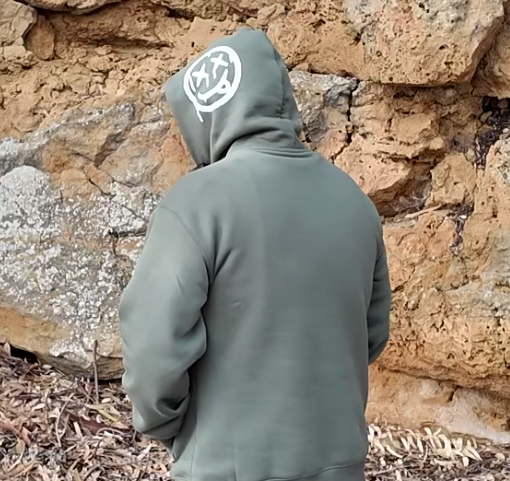 Man wearing a green hoodie with text standing against a stone wall.