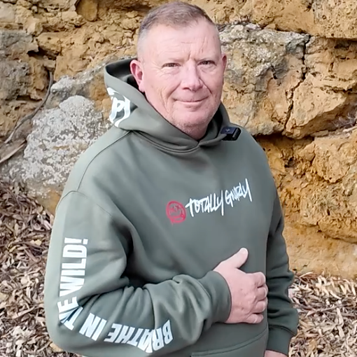 Man wearing a green hoodie with text standing against a stone wall.