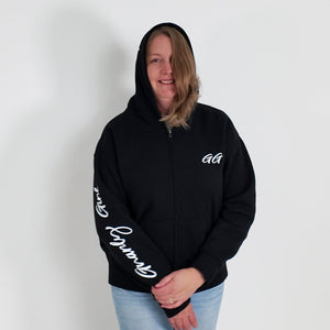 Person wearing a black hoodie with white text, standing against a plain white wall with a plant on the left.